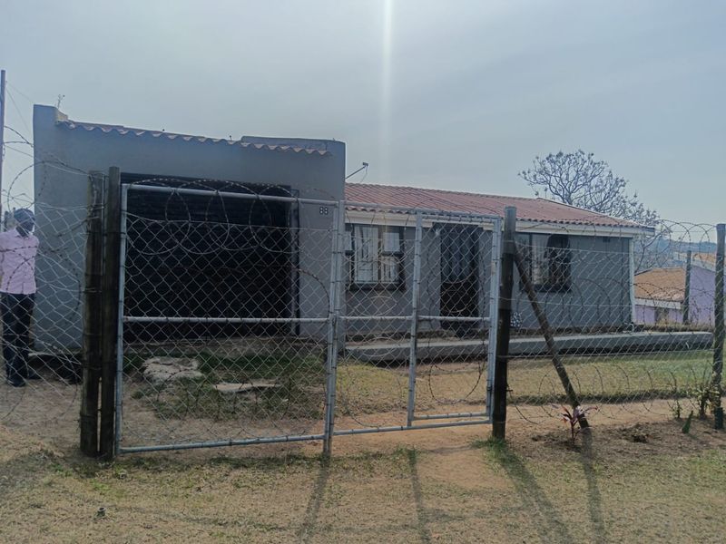 Front exterior view of a single-story house featuring a tiled roof, garage, and secure perimeter fencing with razor wire.