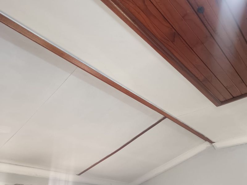 A close-up view of a ceiling featuring white panels with exposed timber beams and decorative coved cornicing.
