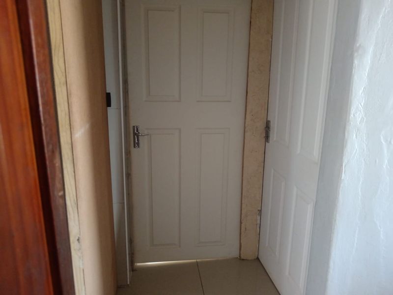 A narrow hallway area featuring white panelled doors and tiled flooring, currently showing signs of unfinished trim and wall detailing.