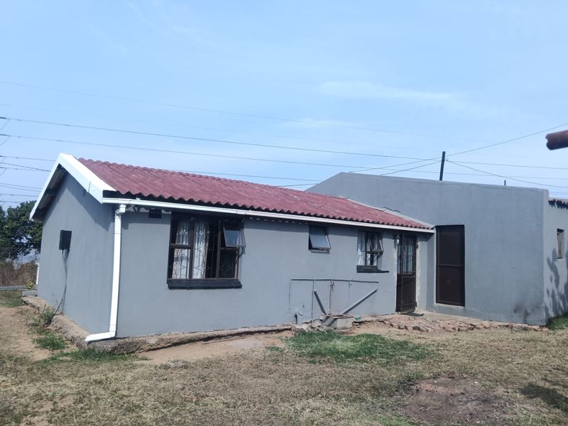 Rear view of a single-story house featuring grey painted walls, a corrugated roof, and security-fitted windows and doors.