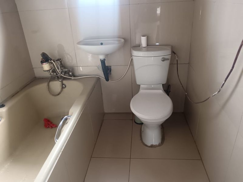 A compact bathroom featuring a bathtub, wall-mounted basin, and toilet with full-height wall tiling.