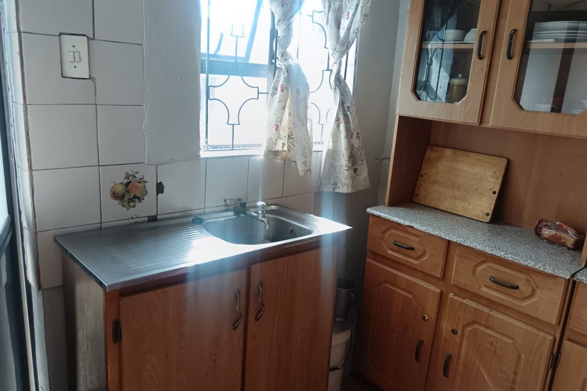 A dated kitchen area featuring wooden cabinetry, a stainless steel sink, and tiled splashbacks with visible wear and maintenance requirements.