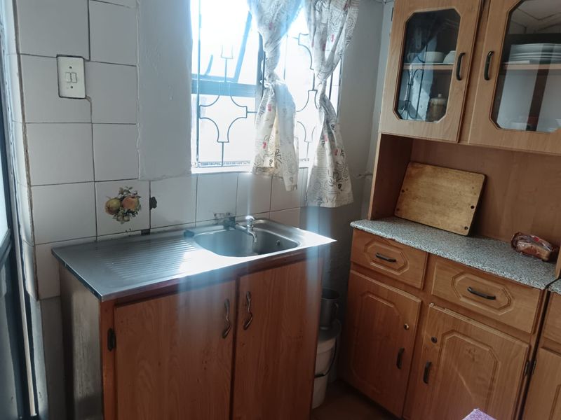 A dated kitchen area featuring wooden cabinetry, a stainless steel sink, and tiled splashbacks with visible wear and maintenance requirements.