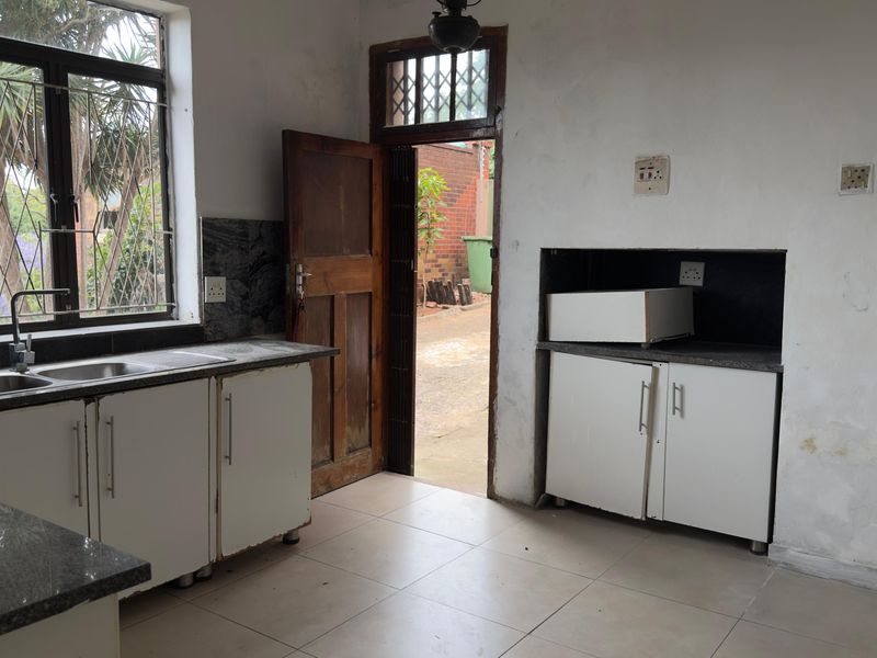 A dated kitchen featuring granite countertops, built-in cabinetry, and tiled flooring, requiring cosmetic updates and wall repairs to improve its overall condition.