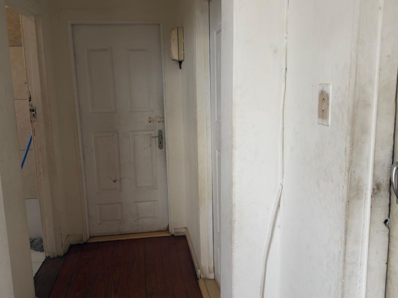 A narrow hallway featuring timber flooring and multiple internal doors, currently showing significant wear and tear on the walls and fixtures.
