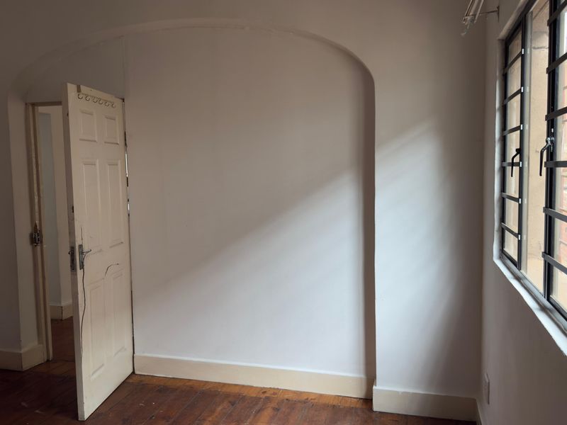 An empty bedroom featuring original timber flooring, an arched wall recess, and a window fitted with security bars.
