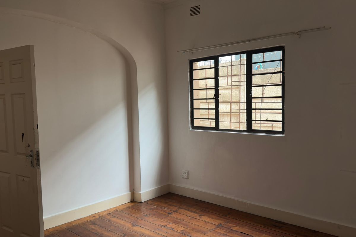 An empty bedroom featuring original timber flooring, an arched architectural detail, and a window fitted with security bars.