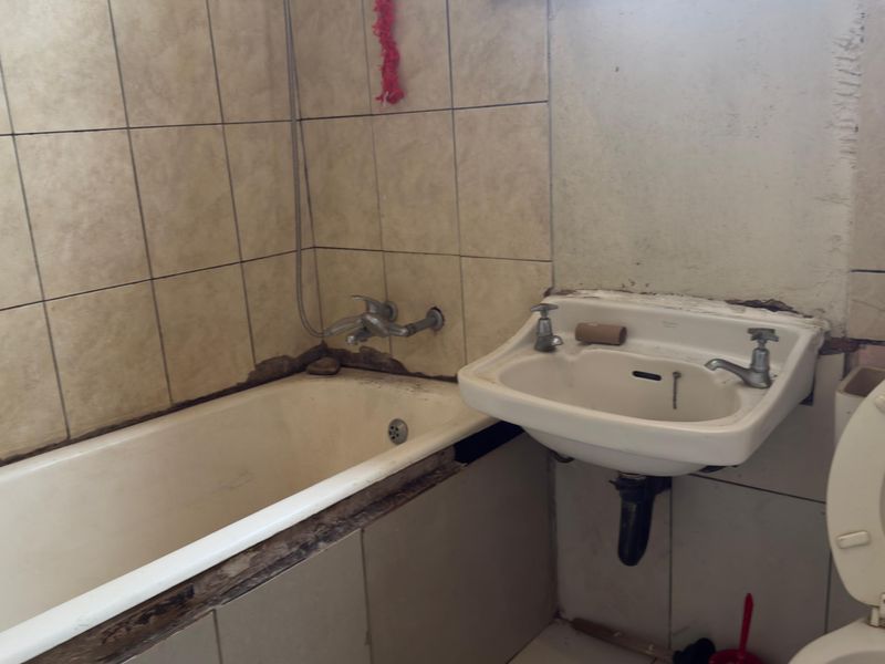 A dated bathroom featuring a bathtub, wall-mounted basin, and toilet, requiring significant maintenance and cosmetic updates to the tiling and wall finishes.