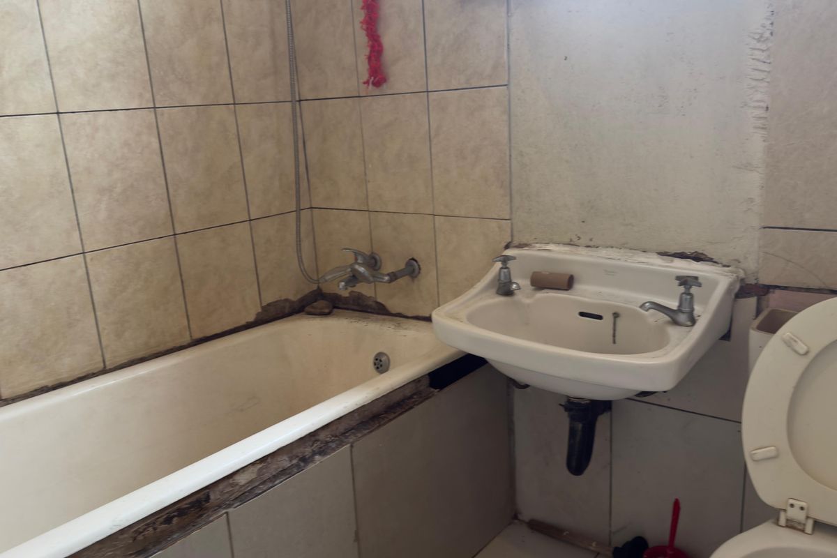 A dated bathroom featuring a bathtub, wall-mounted basin, and toilet, requiring significant maintenance and cosmetic updates to the tiling and wall finishes.