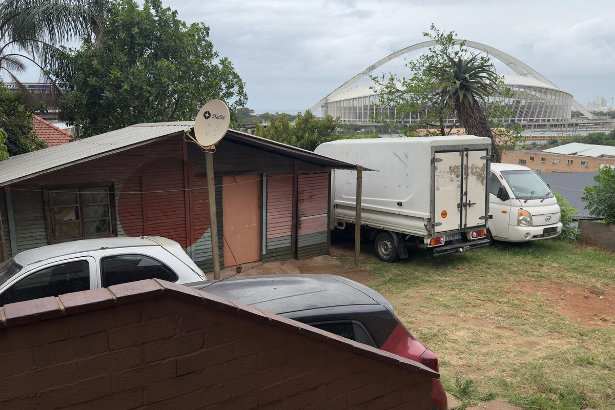 Rear exterior view of a property featuring a structure with corrugated metal roofing and timber cladding, situated in a residential area.