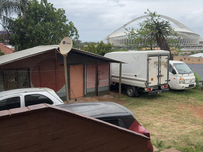 Rear exterior view of a property featuring a structure with corrugated metal roofing and timber cladding, situated in a residential area.