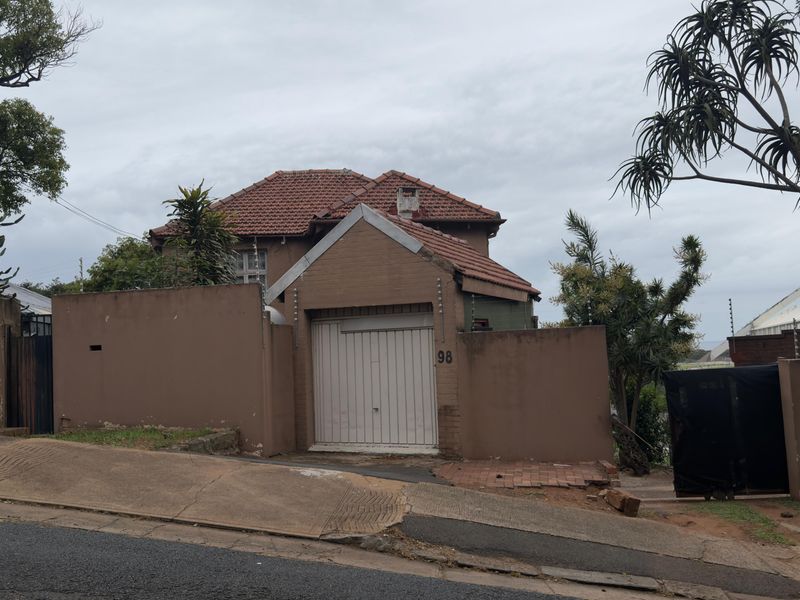 Front elevation of a residential property featuring a brick boundary wall, tiled roof, and integrated garage, situated on a sloped street.