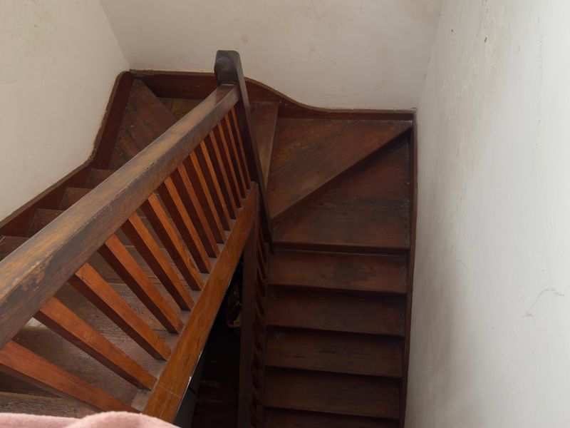 A traditional wooden staircase featuring a classic balustrade and handrail, showing signs of wear and requiring cosmetic refurbishment.