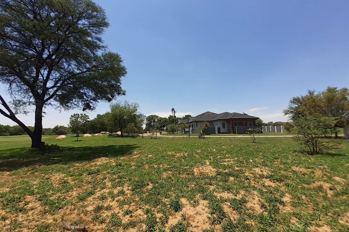 A spacious residential plot featuring established trees, open lawn areas, and a clear view of the adjacent property structure.