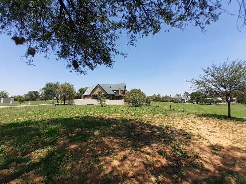 A wide-angle view of a residential vacant land plot featuring established trees, a boundary wall, and a view of the neighboring property.