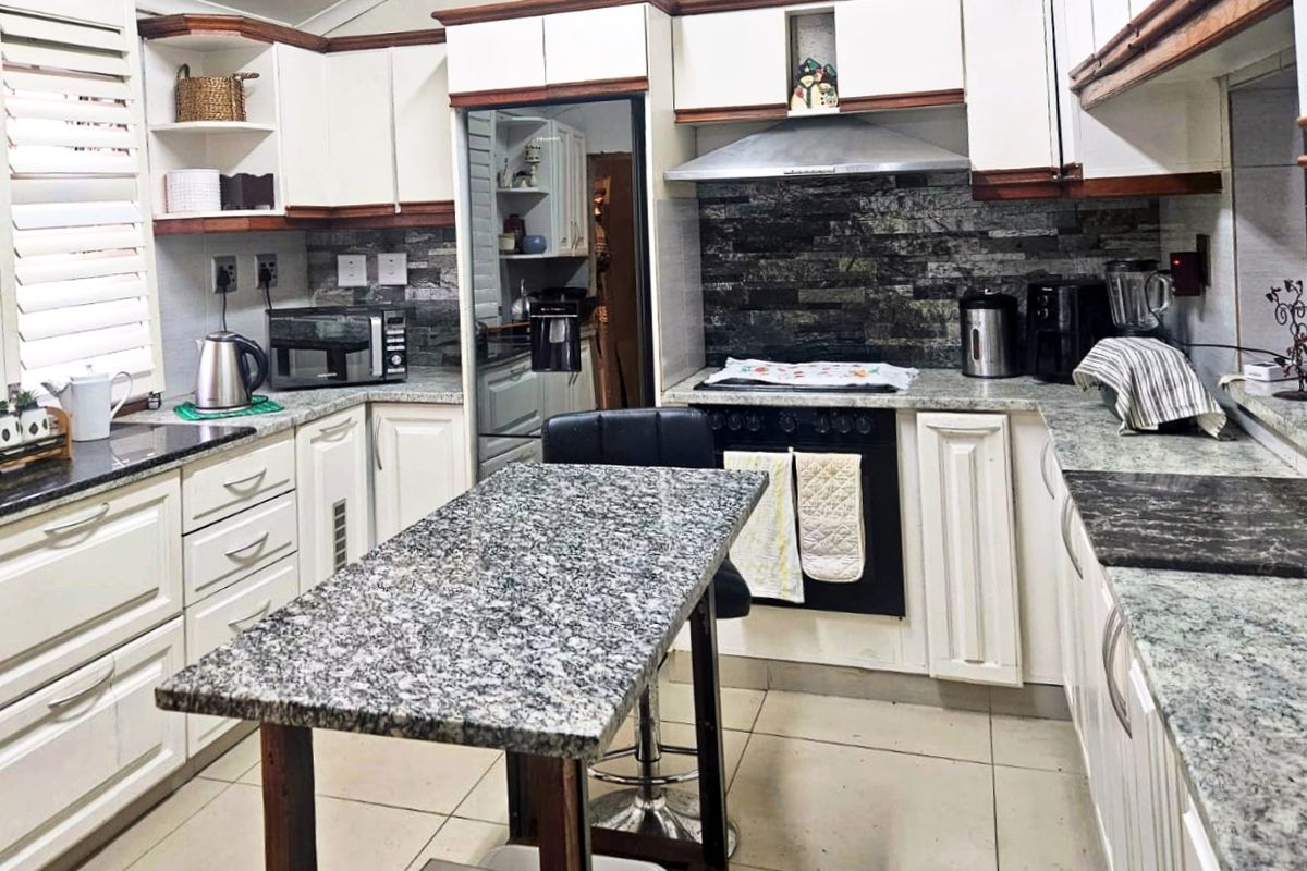 A functional kitchen featuring granite countertops, white cabinetry with wood trim, a stone tile backsplash, and a central island workspace.