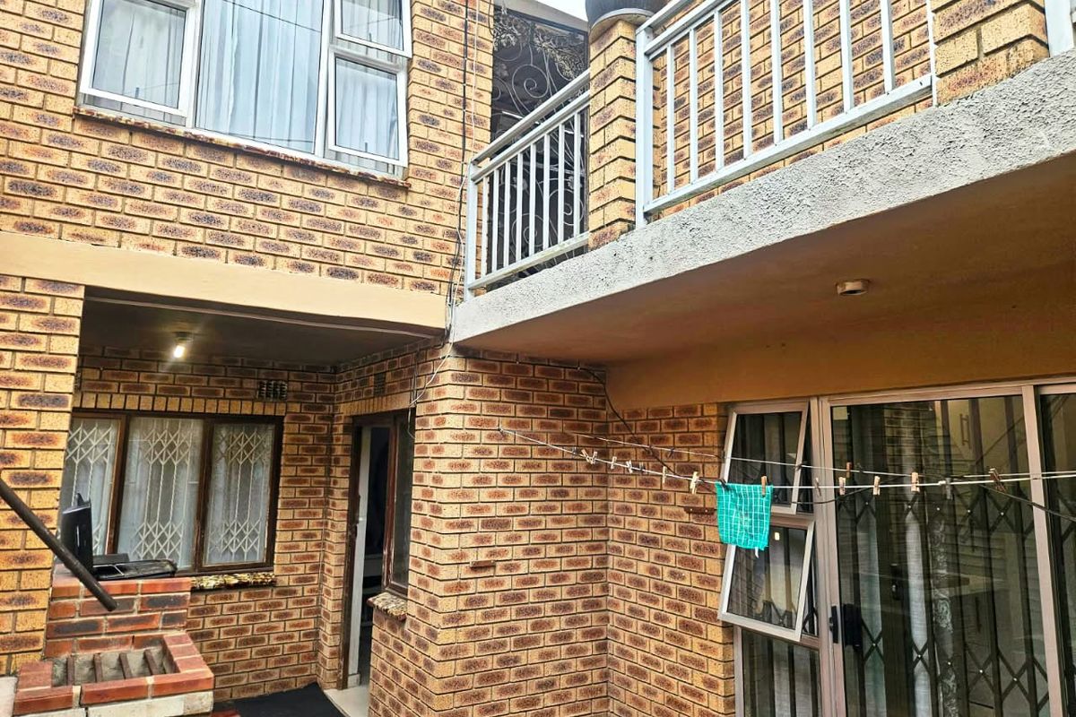 Rear exterior view featuring a face brick facade, a balcony with metal railings, sliding glass doors, and a built-in brick braai area.