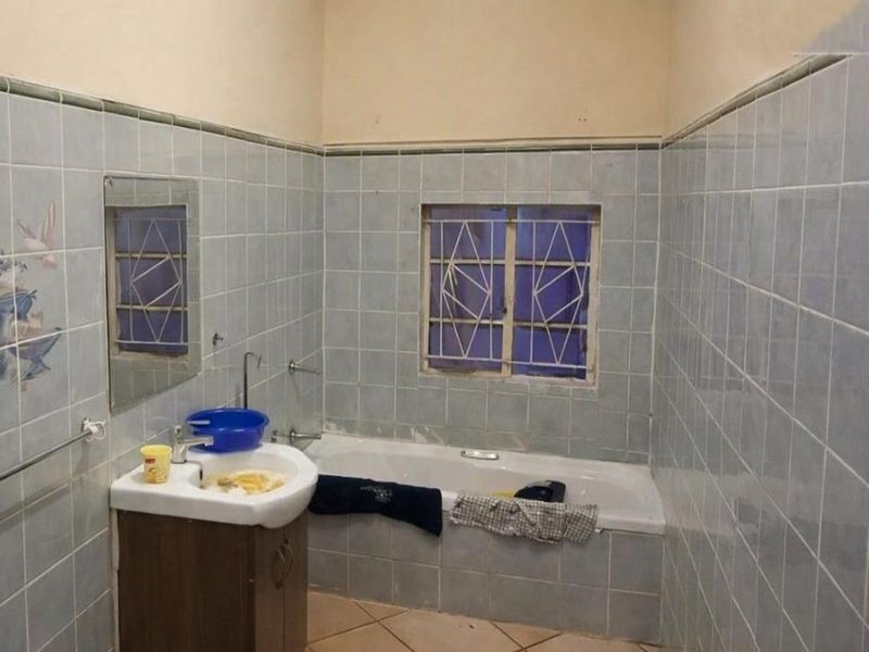 A dated bathroom featuring a built-in bathtub, vanity basin, and full-height wall tiling, requiring cosmetic updates to modernize the space.