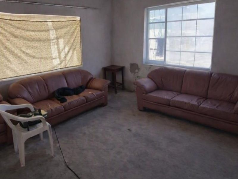 A living room space featuring concrete flooring and aluminium windows, currently requiring significant wall finishing and plaster repairs.