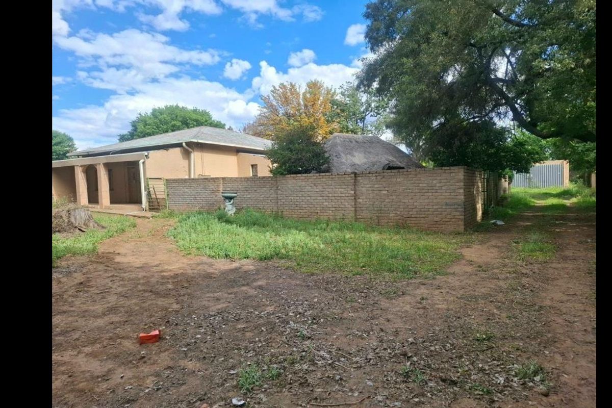 Rear view of the property featuring a brick boundary wall, a thatched roof structure, and a covered patio area with surrounding unpaved garden space.