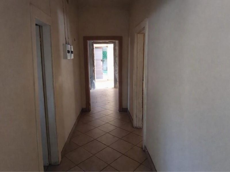 A vacant interior hallway featuring tiled flooring and visible electrical infrastructure, leading towards an exterior doorway.