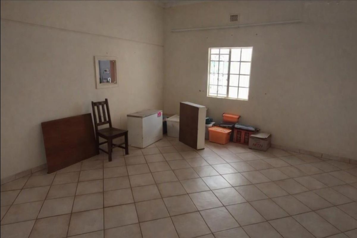 A vacant living area featuring neutral tiled flooring and a window with security bars, offering a blank canvas for potential renovation or staging.