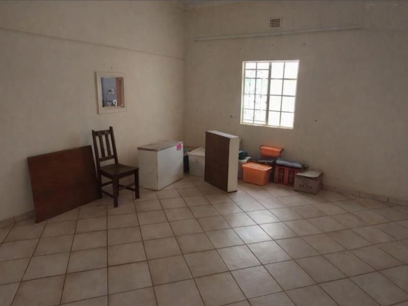 A vacant living area featuring neutral tiled flooring and a window with security bars, offering a blank canvas for potential renovation or staging.