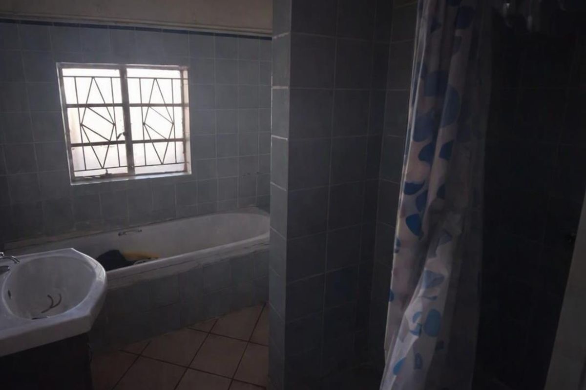 A dated bathroom featuring a built-in bathtub, wall-mounted basin, and tiled finishes, requiring modernization to improve its aesthetic and functionality.