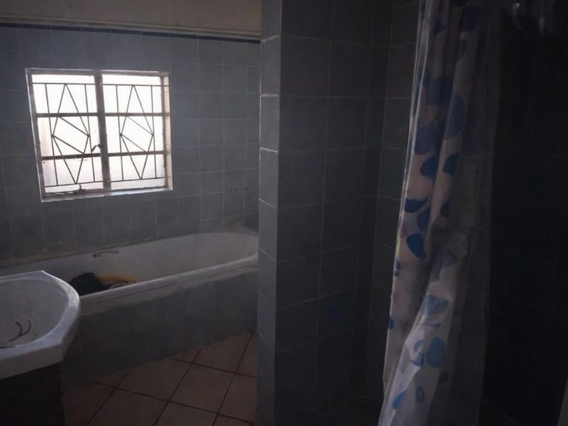 A dated bathroom featuring a built-in bathtub, wall-mounted basin, and tiled finishes, requiring modernization to improve its aesthetic and functionality.