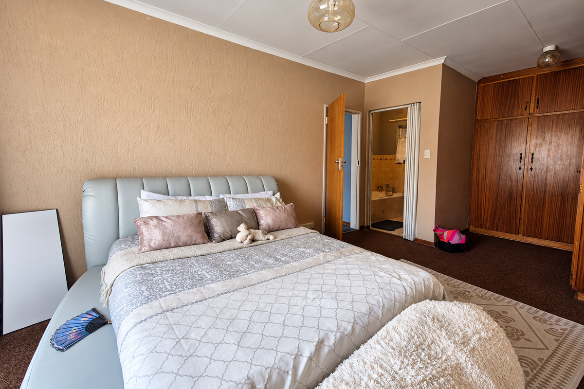 Spacious bedroom featuring built-in wooden cupboards, textured walls, and direct access to an en-suite bathroom.