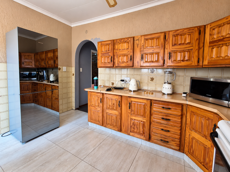 A dated kitchen featuring traditional wooden cabinetry, tiled backsplash, and tiled flooring, with an arched doorway leading to an adjacent space.