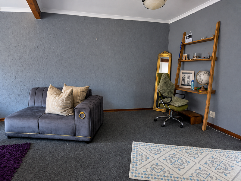 A living room area featuring grey textured walls, carpeted flooring, and an exposed timber ceiling beam.