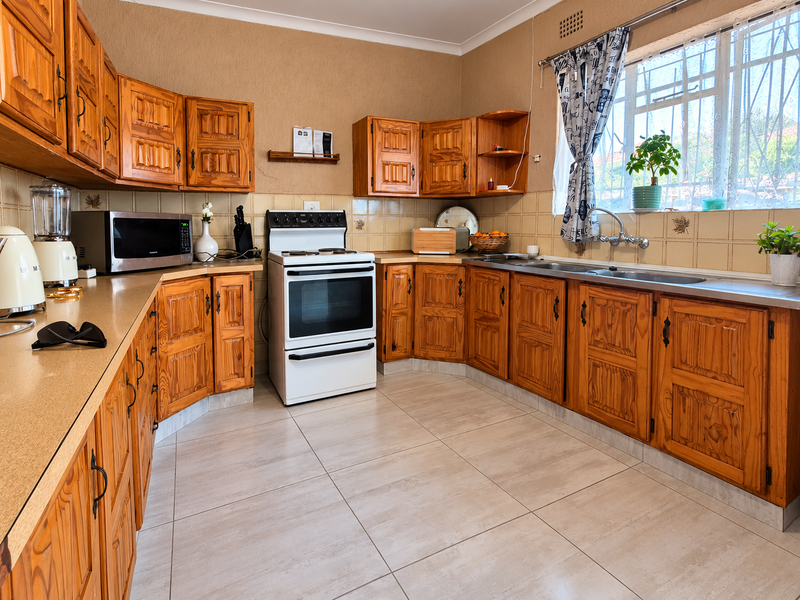 A functional kitchen featuring traditional wooden cabinetry, laminate countertops, a freestanding stove, and a double basin sink with tiled backsplash and flooring.