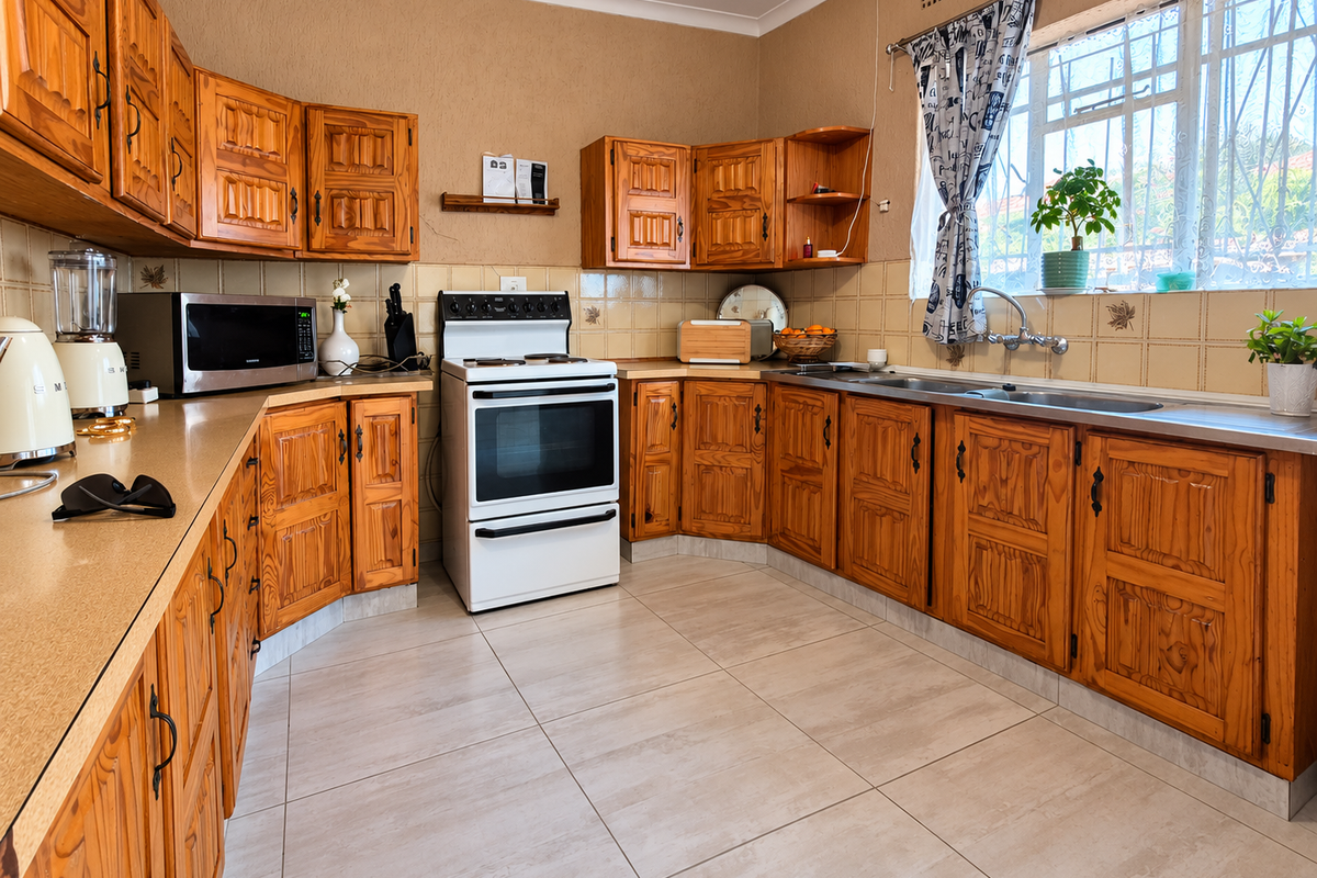 A functional kitchen featuring traditional wooden cabinetry, laminate countertops, a freestanding stove, and a double basin sink with tiled backsplash and flooring.