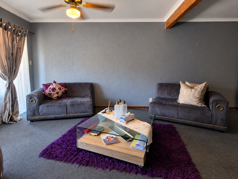 A living room featuring grey textured walls, a ceiling fan, an exposed timber beam, and sliding glass door access to the exterior.