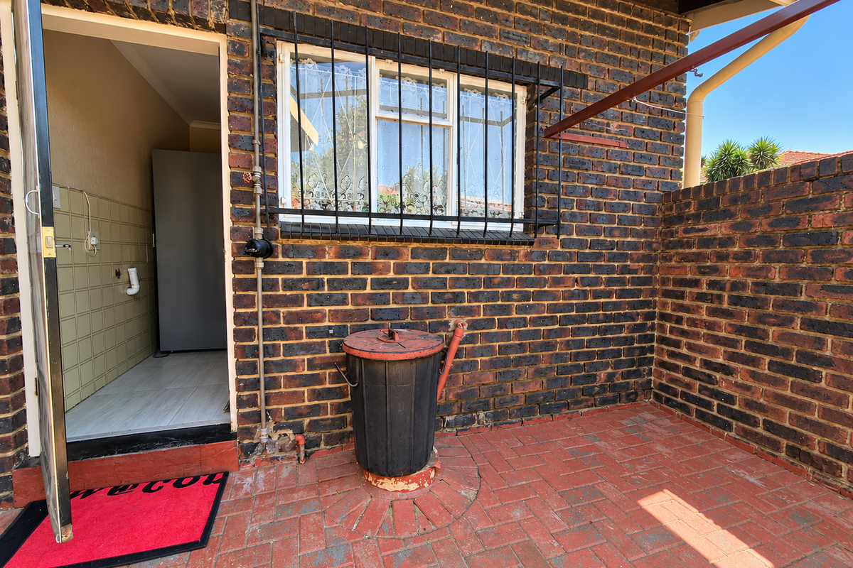 Rear exterior view of a townhouse featuring a face brick facade, security bars on the window, and a paved patio area.