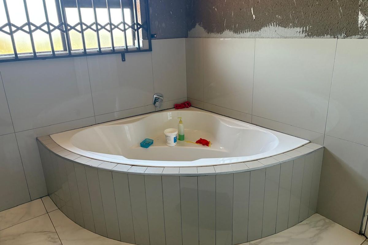 A bathroom featuring a corner bathtub with tiled surround and flooring, currently undergoing renovation with unfinished wall plastering visible.