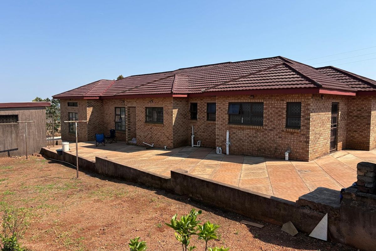 Rear view of a face brick house featuring a tiled roof, paved patio area, and a retaining wall overlooking the garden.