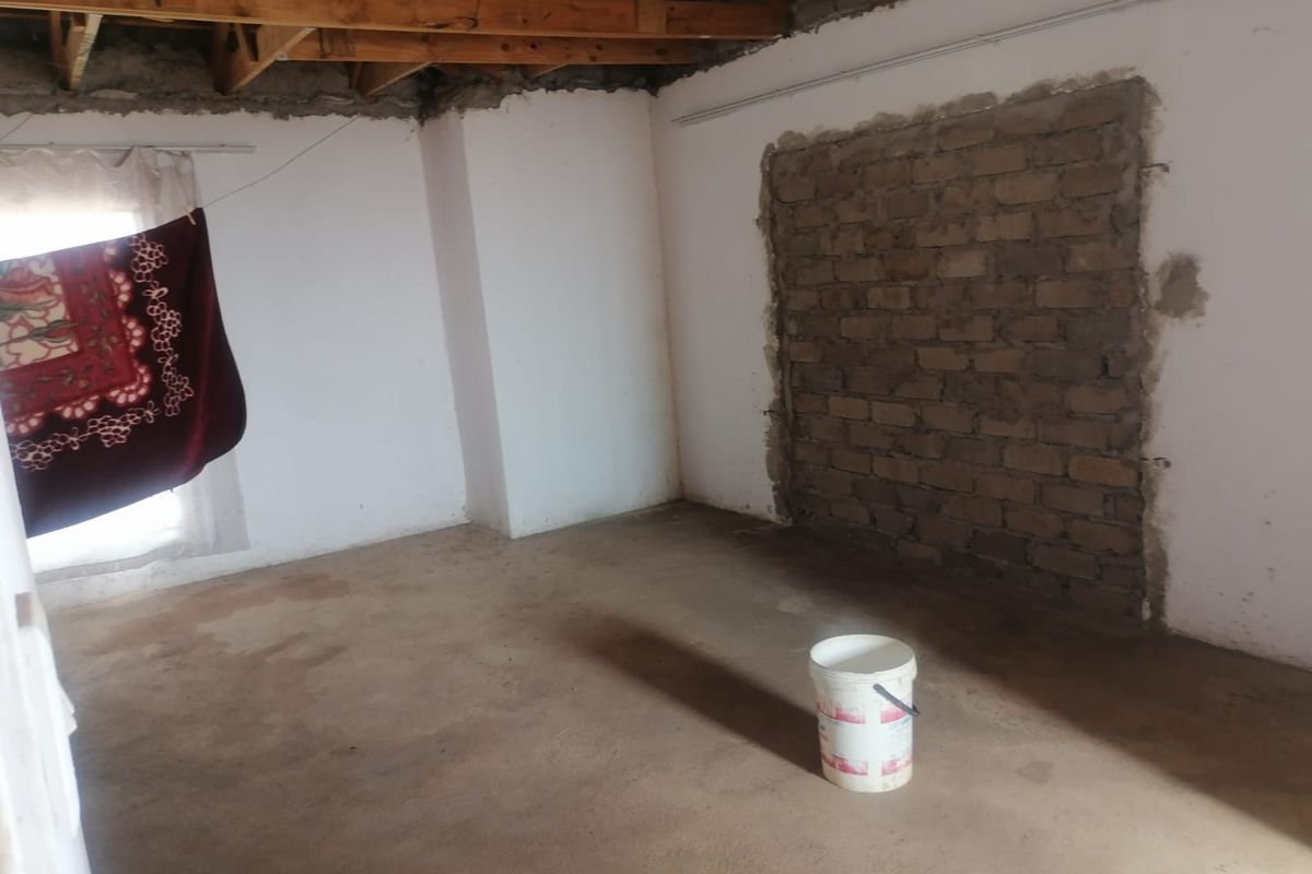 An unfinished room featuring exposed timber ceiling beams, raw brickwork, and concrete flooring, offering a blank canvas for renovation and interior design.