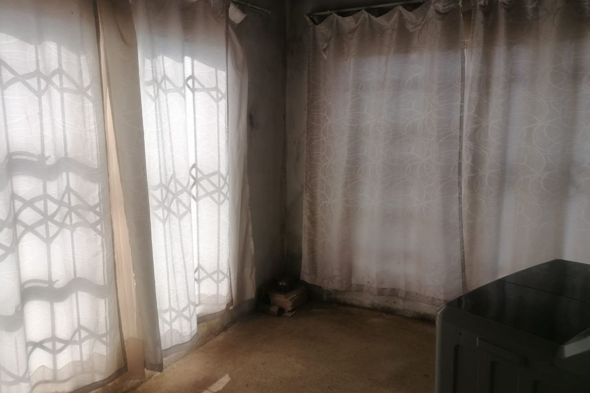 An empty room featuring unfinished wall surfaces and security gates on the windows, requiring significant renovation and cosmetic updates.