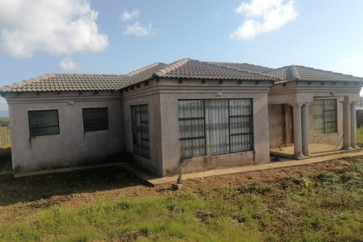 Front elevation of a single-story house featuring a tiled roof, concrete columns, and security bars on windows, set on an unlandscaped plot.