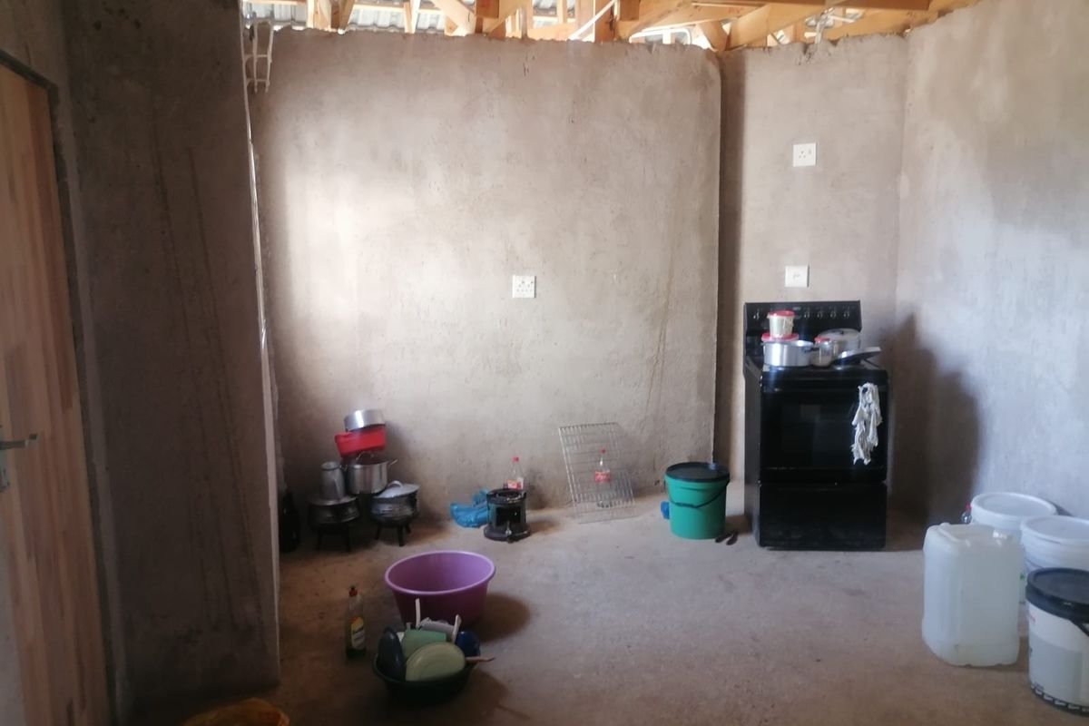 An unfinished kitchen area featuring exposed timber roof trusses, raw cement walls, and a freestanding stove, awaiting completion and installation of cabinetry.