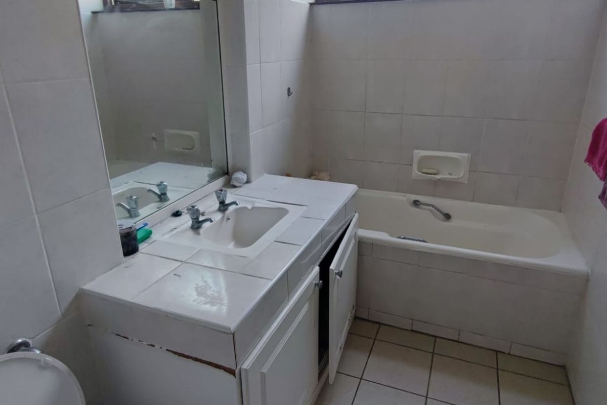 A functional bathroom featuring a tiled bathtub, vanity with basin, and wall-mounted mirror, requiring some cosmetic updates to the cabinetry and finishes.