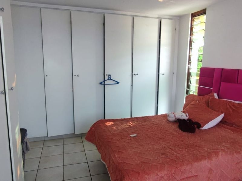 A bedroom featuring extensive built-in cupboards, tiled flooring, and louvre windows, providing functional storage and natural light.