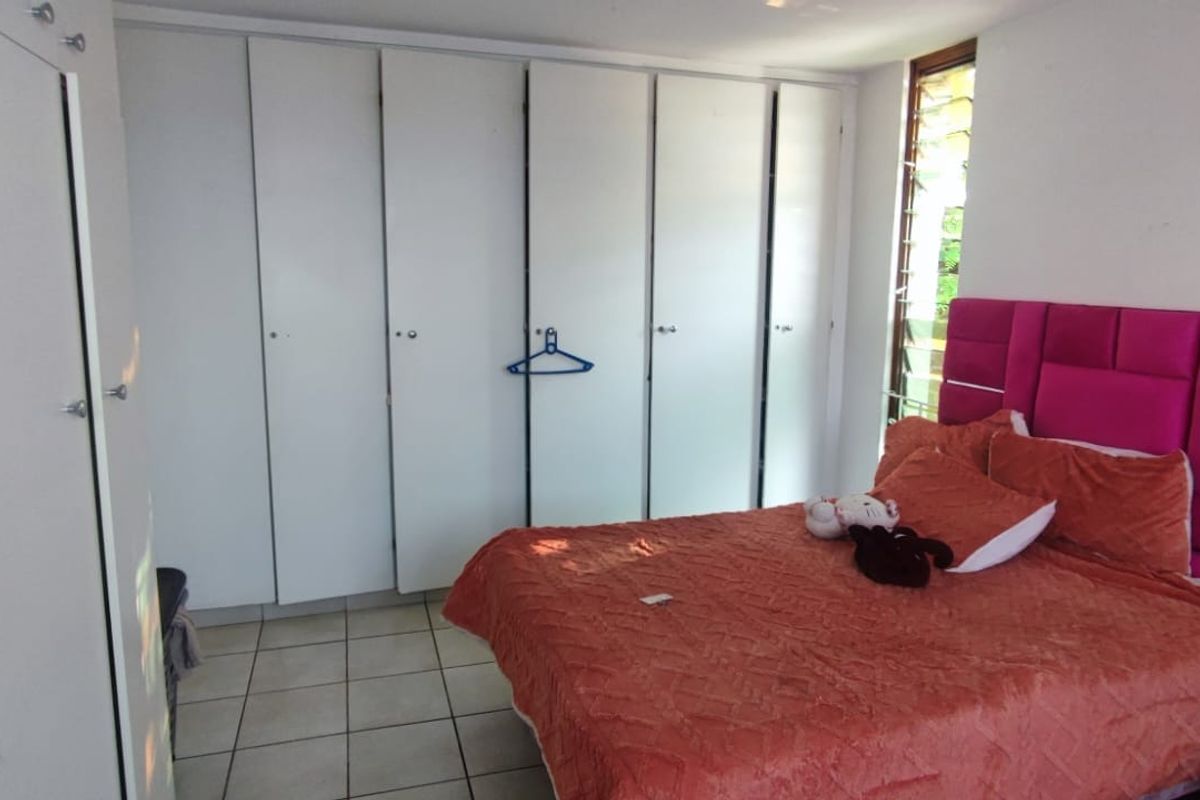 A bedroom featuring extensive built-in cupboards, tiled flooring, and louvre windows, providing functional storage and natural light.