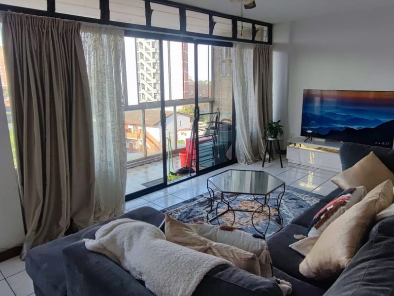 A bright living room featuring tiled flooring and large sliding glass doors that provide access to the balcony and natural light.