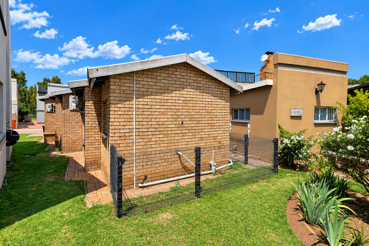 Rear exterior view of the townhouse featuring brick construction, a small fenced utility area, and landscaped garden space.