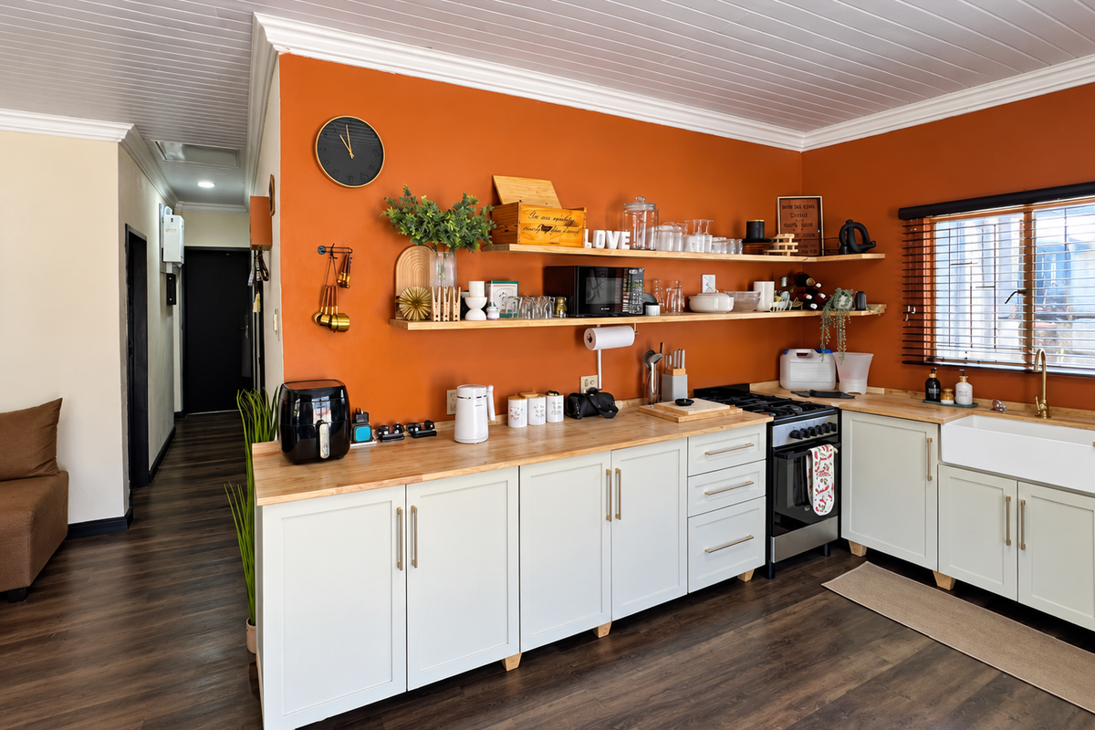 A well-maintained kitchen featuring shaker-style cabinetry, butcher block countertops, an apron-front sink, and open shelving against a vibrant orange feature wall.