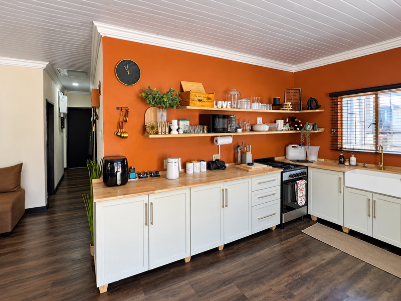 A well-maintained kitchen featuring shaker-style cabinetry, butcher block countertops, an apron-front sink, and open shelving against a vibrant orange feature wall.