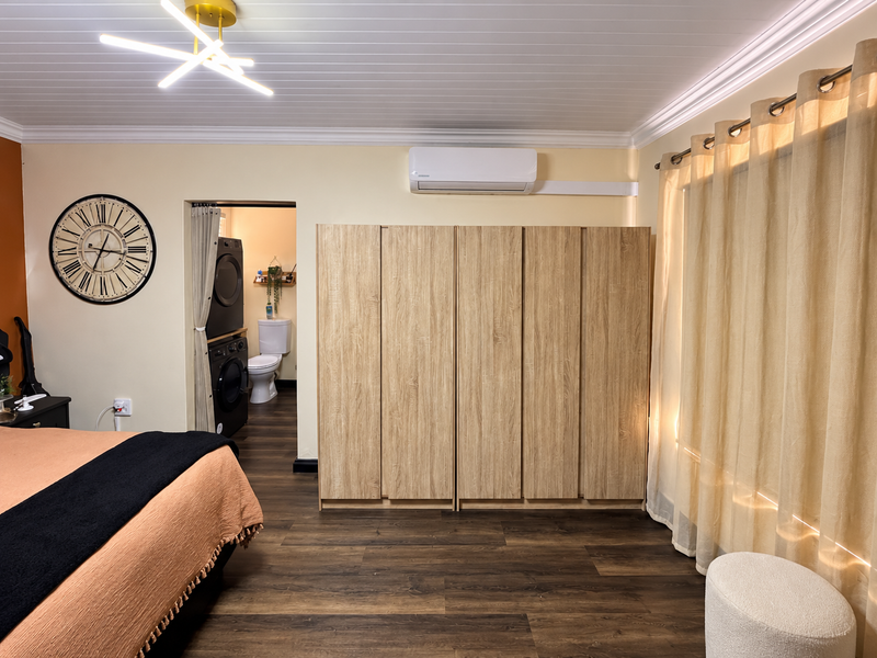 A well-maintained bedroom featuring built-in wooden wardrobes, split-system air conditioning, laminate flooring, and direct access to an en-suite bathroom.